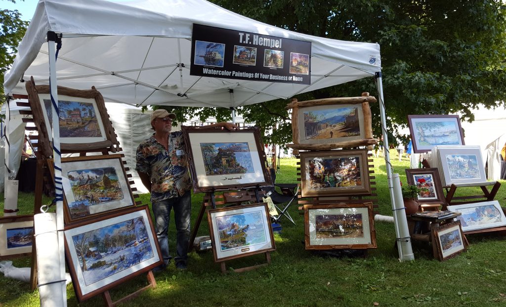 Tom Hempel standing with his paintings at the River Renaissance Festival.